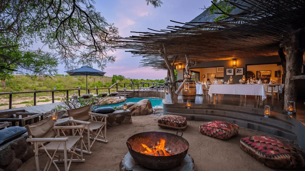 Fire pit, pool and lit main deck at Jock Safari Lodge at dusk