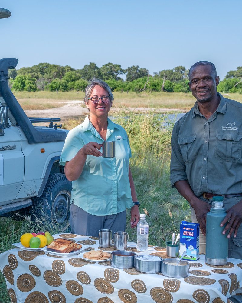 Guest and guide at a bush breakfast beside a safari vehicle in the Okavango Delta