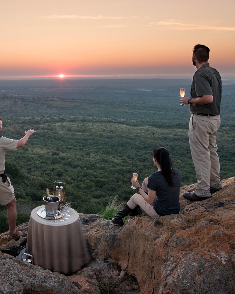 Guests at sundowners on a rocky outcrop above the Phinda reserve at sunset