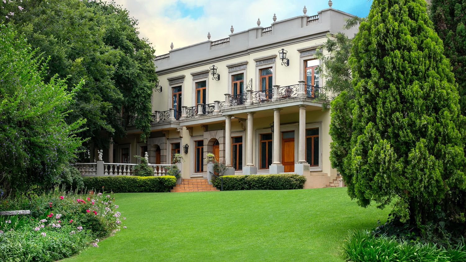 The main house at Fairlawns Boutique Hotel and Spa seen across its lawn, a white colonnaded manor in landscaped gardens