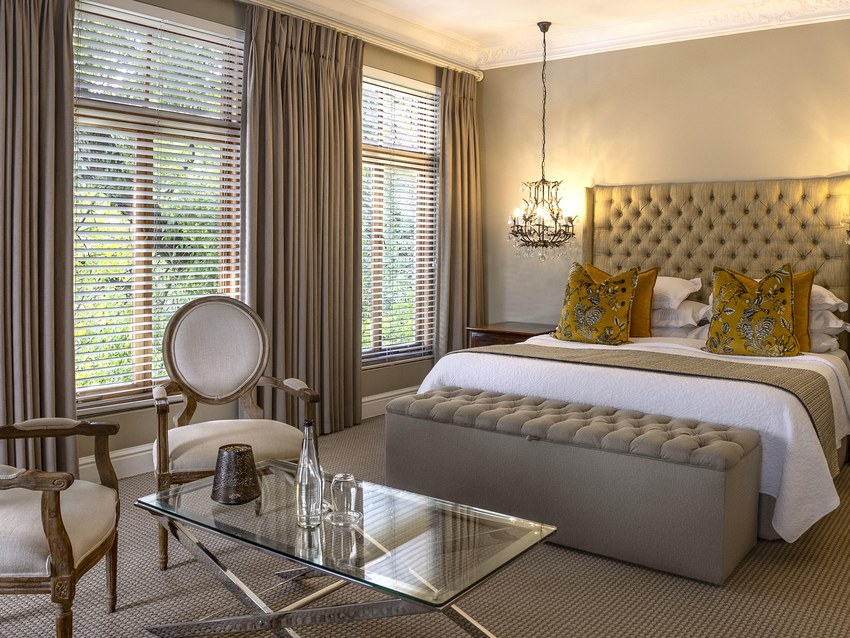 A suite bedroom at Fairlawns with an upholstered headboard, armchair and shuttered windows