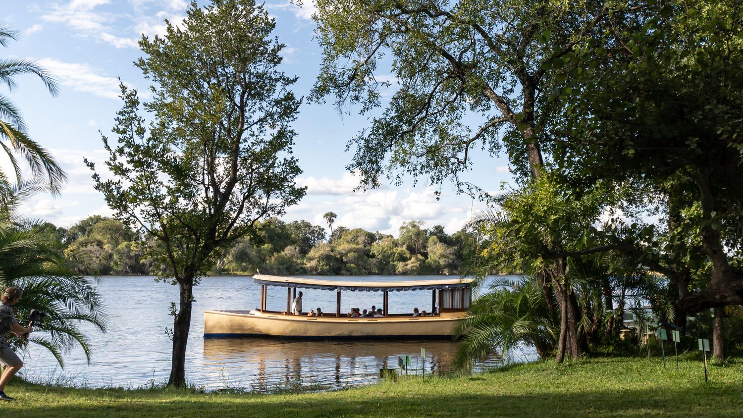 The Palm River Hotel seen across its lawn with the Zambezi River and a moored river boat beyond