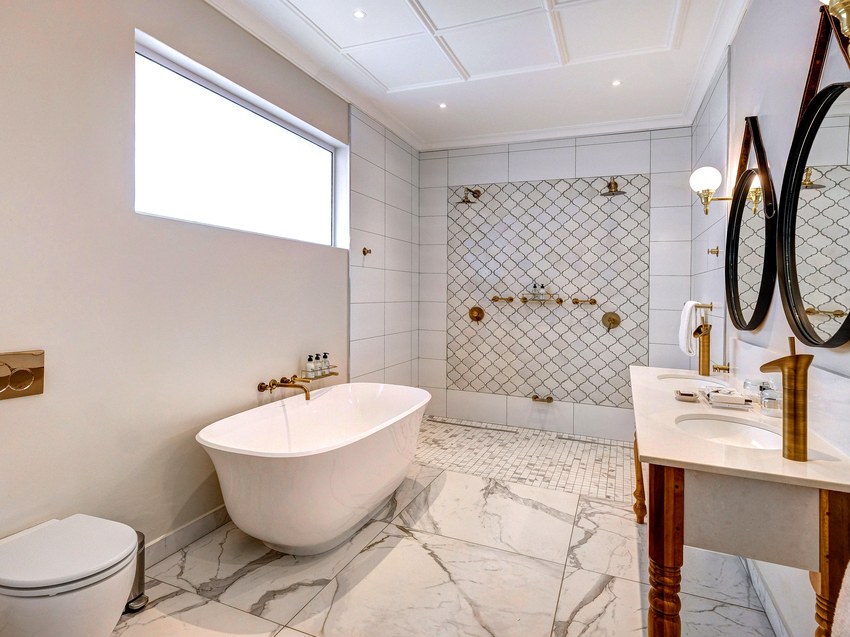 A bathroom at the Palm River Hotel with a freestanding bath, marble floor and twin round mirrors