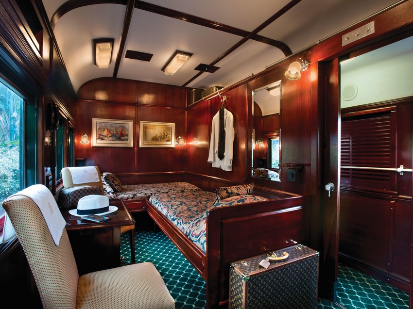 A wood-panelled Rovos Rail suite in daytime configuration with a sofa seat, armchair and window