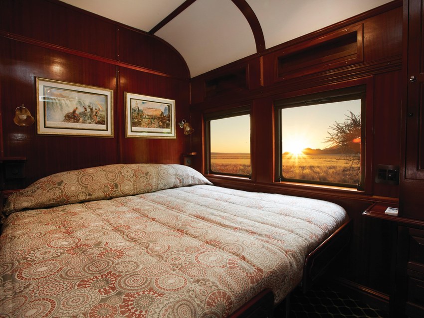 A Rovos Rail suite made up for the night with a double bed beneath two windows at sunset