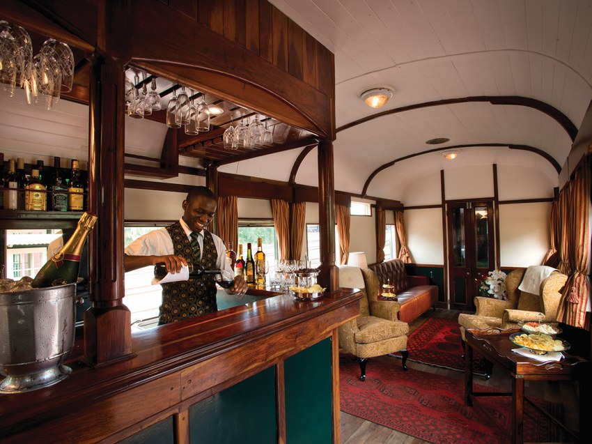The bar aboard Rovos Rail with a steward serving, wine glasses overhead and a champagne bucket
