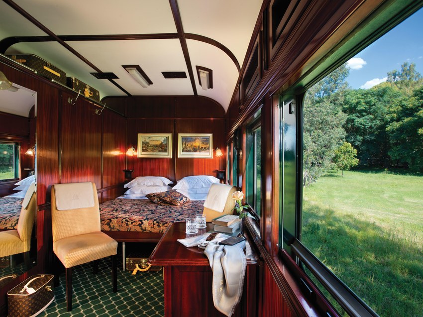 A table laid for a meal beside the window of a Rovos Rail carriage, with the countryside passing outside