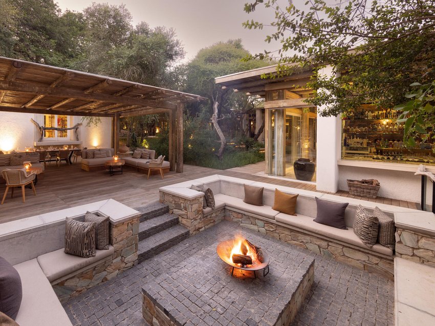 The outdoor fire pit lounge at Kapama Karula lit at dusk, with sunken seating around an open fire
