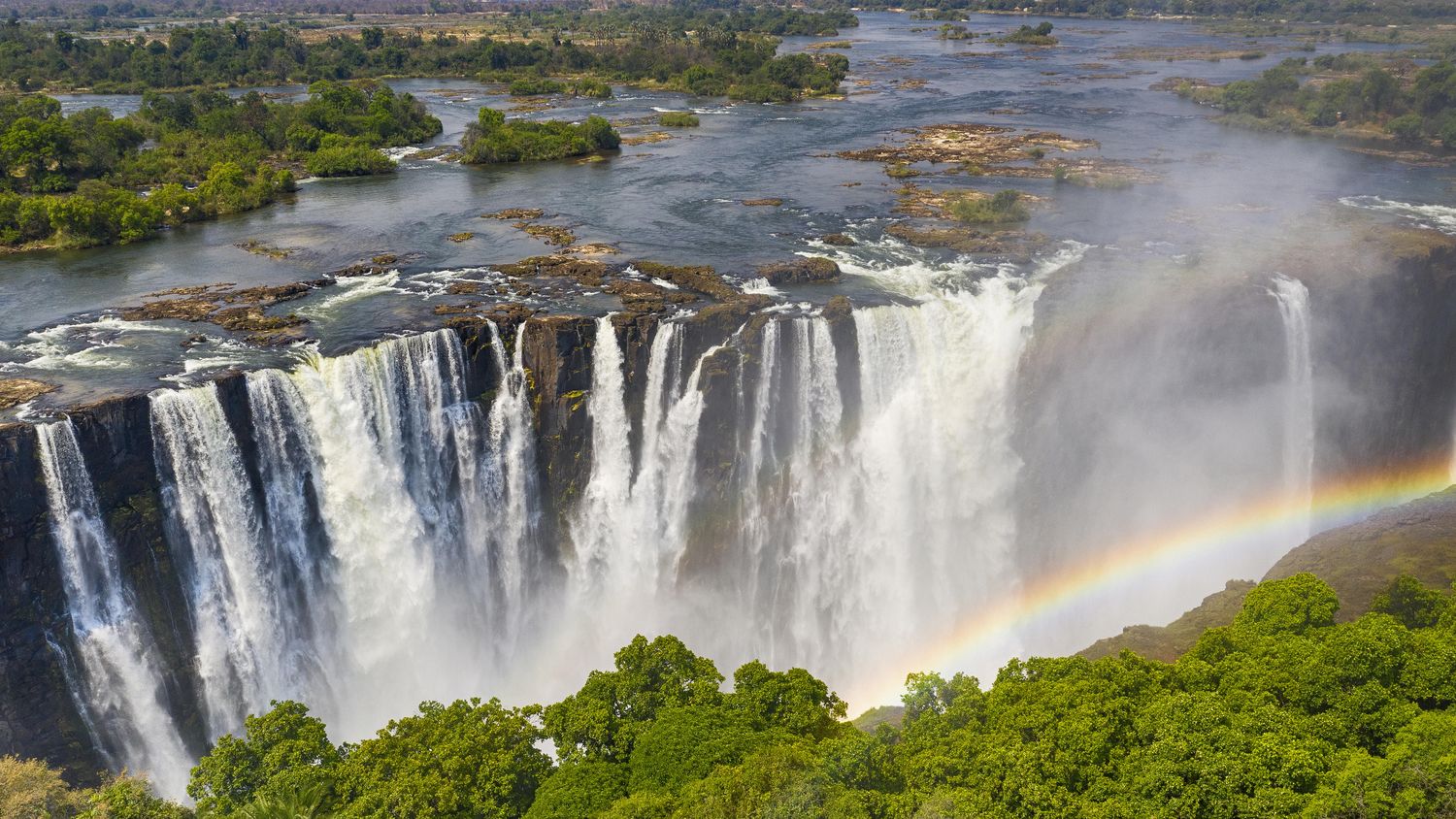 Aerial view of Victoria Falls in full flow with a rainbow over the gorge
