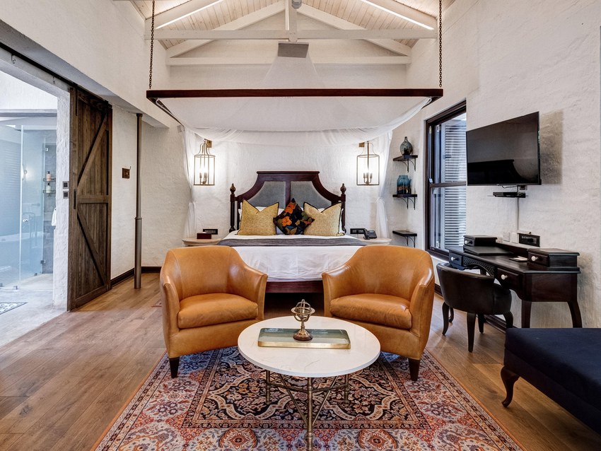 A Deluxe King suite at Mbano Manor Hotel with a king bed, separate lounge chairs and a writing desk under a vaulted ceiling