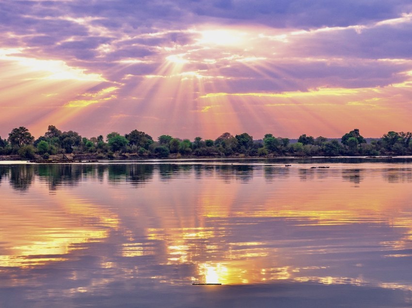 Sunset over the Zambezi River with rays of light through cloud reflected in still water