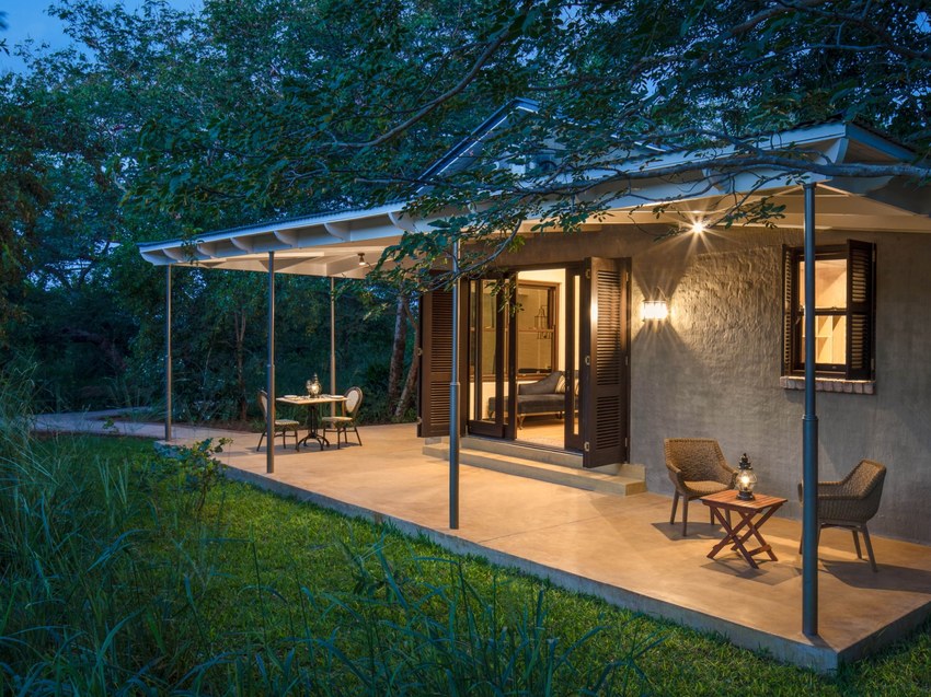 A suite at Mbano Manor lit at dusk, seen from the forest path that runs between the suites