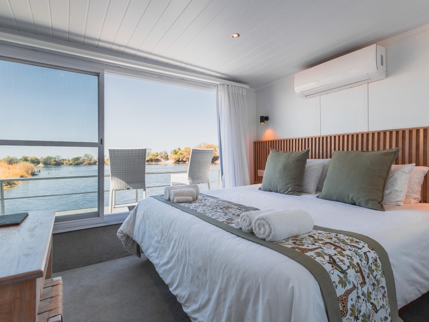 A cabin aboard the Chobe Princess with a double bed and full-height windows sliding open onto the river