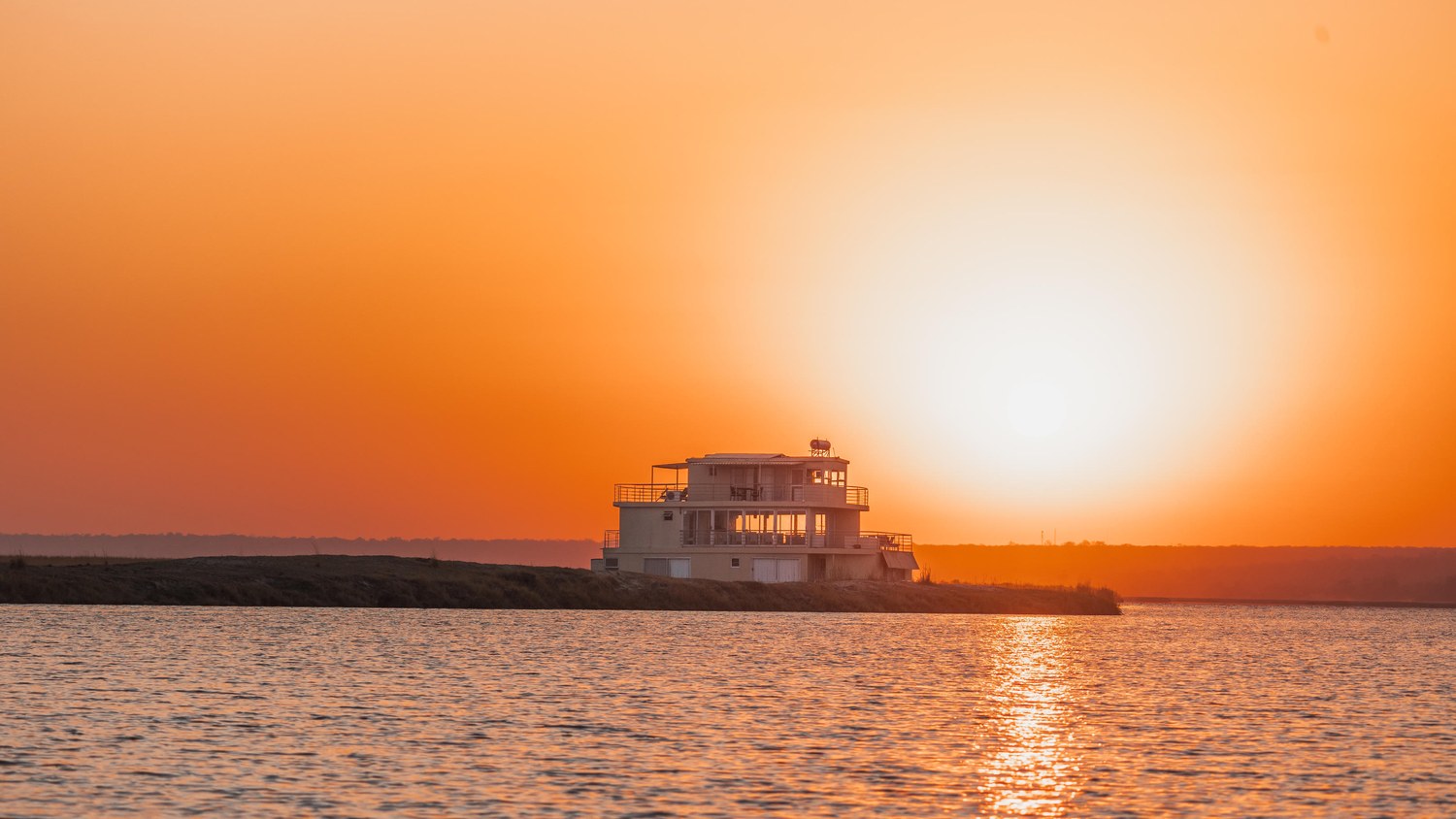Sunset over the Chobe River with the houseboat silhouetted against the water