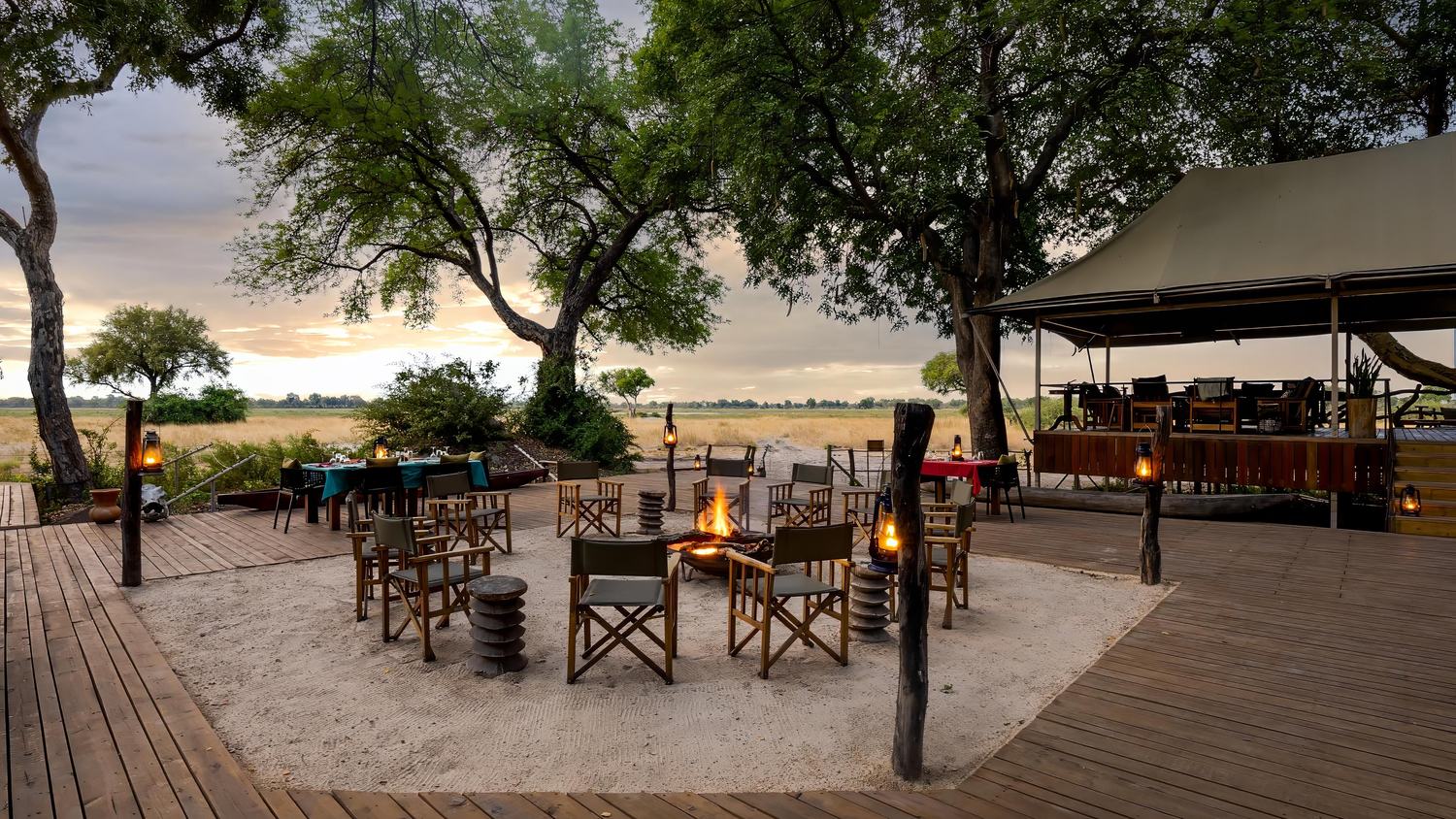 The open deck and fire circle at Kadizora Camp at dusk, with camp chairs set out under the trees