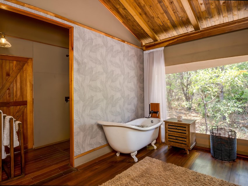 An en-suite tent bathroom at Kadizora Camp with a freestanding claw-foot bath beside a window onto the bush