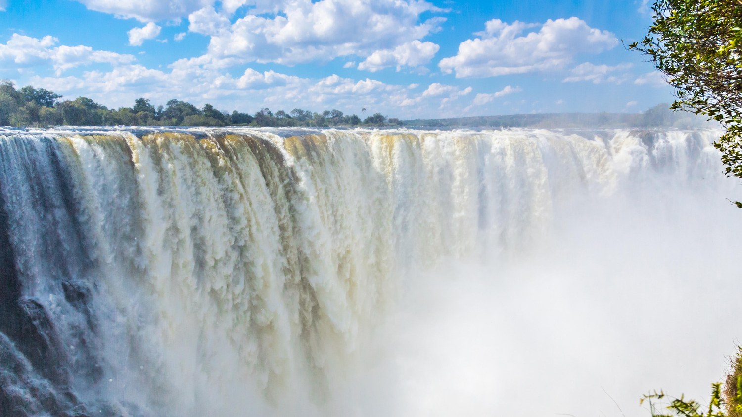 Victoria Falls in full flow, the curtain of water stretching across the gorge under a blue sky