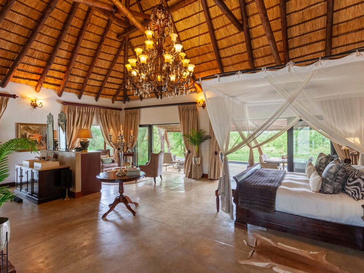 Thatched suite interior with four-poster bed and chandelier at Kings Camp