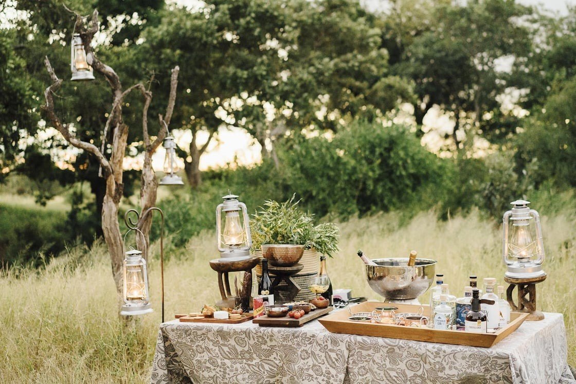 Drinks and lanterns set out on a table in the bush before sunset