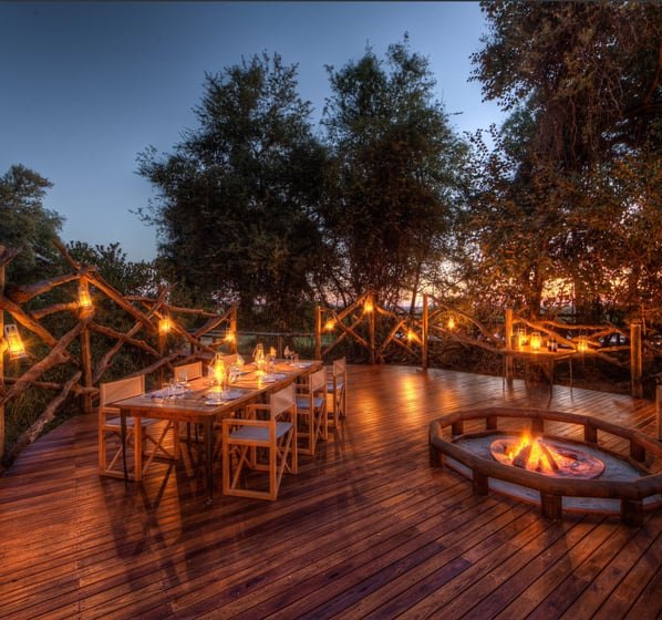 Fire-lit dinner table on a raised deck in the Botswana bush