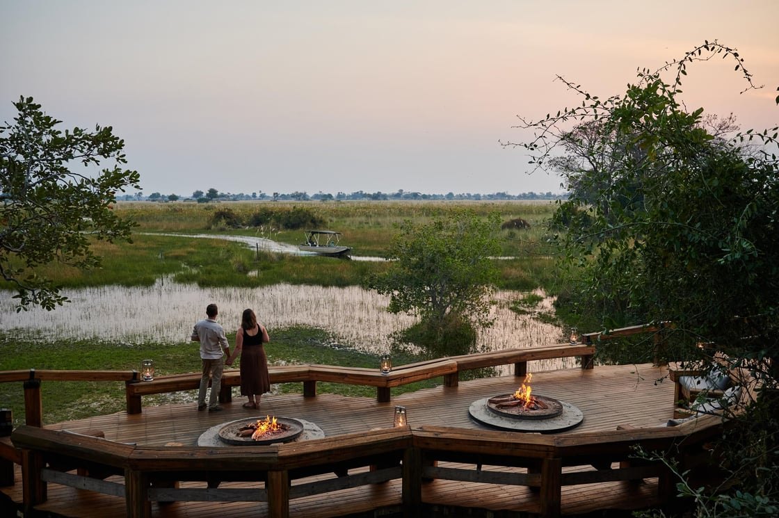 Guests on a camp deck with fire pits overlooking an Okavango floodplain